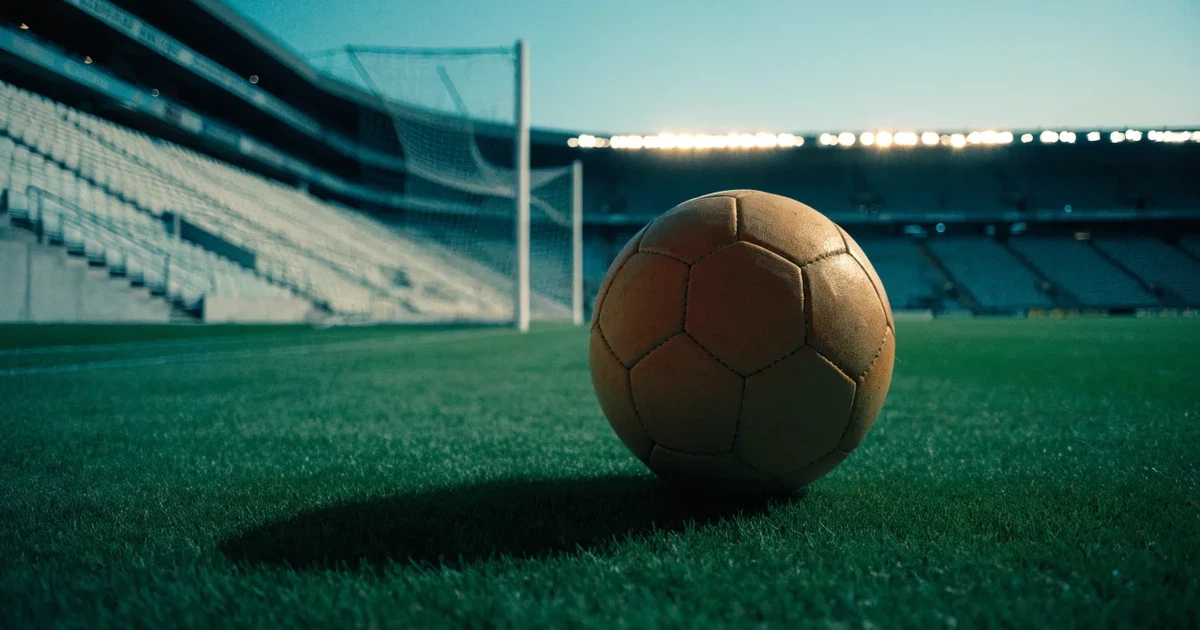 Ein Fußball liegt im Strafraum direkt vor dem Tor mit Netz, im Hintergrund leere Ränge bei Dämmerung.