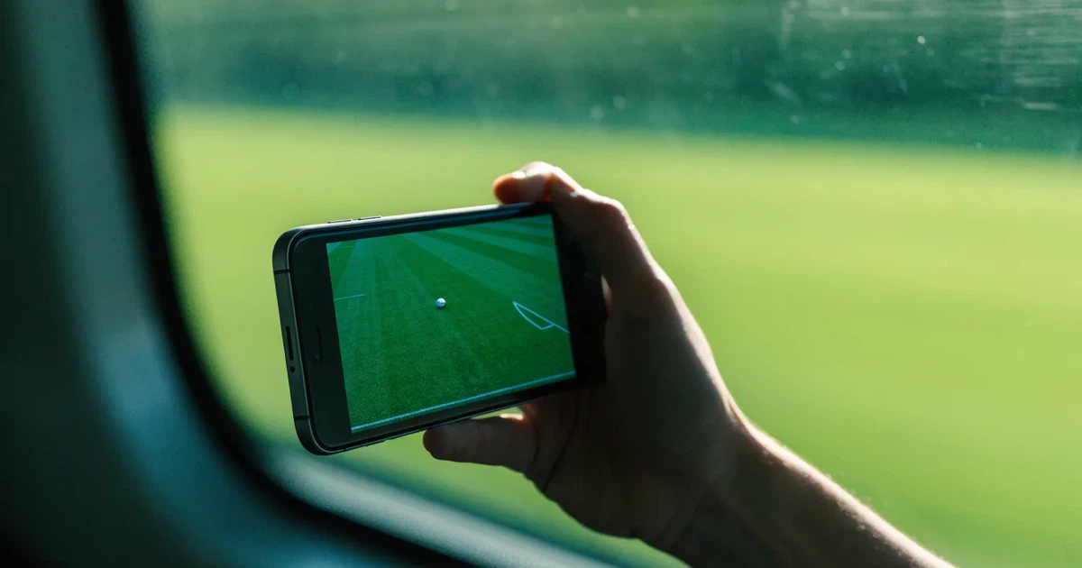 Eine Hand hält ein Smartphone mit dunklem Display in einem Zug, am Fenster ziehen verschwommen Felder vorbei.