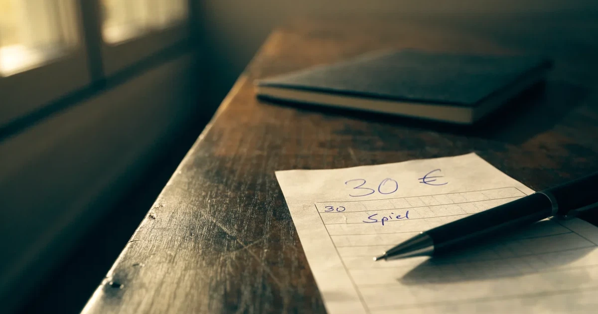 Ein leerer Papier-Wettschein und ein Kugelschreiber liegen auf einem Tisch, daneben ein kleiner Stapel Münzen.