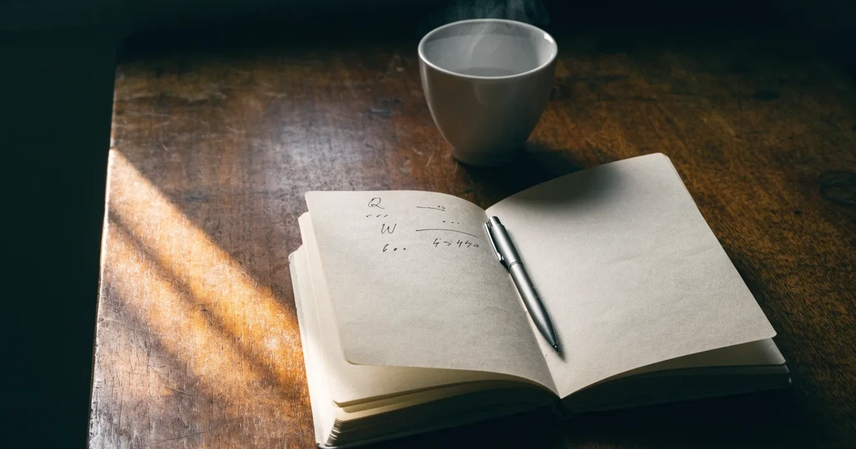 Ein Notizbuch mit handschriftlichen Rechnungen und ein Taschenrechner liegen auf einem Schreibtisch neben einer Tasse Kaffee im Licht des frühen Morgens.