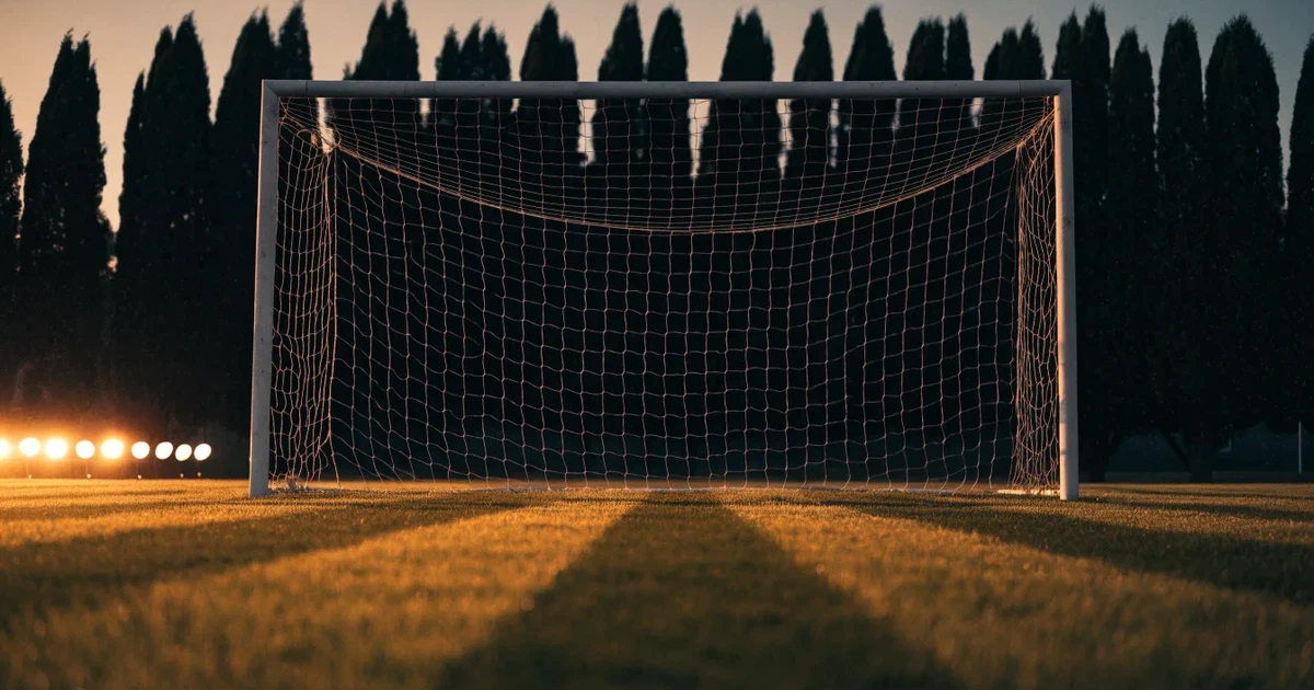 Ein Fußballtor mit Netz auf einem leeren Platz im Abendlicht, der Rasen frisch gemäht, im Hintergrund Zypressen.