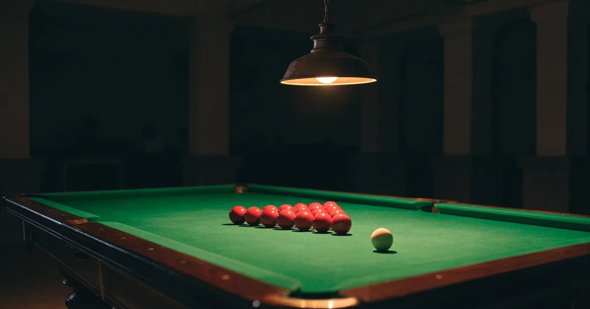 Ein Snookertisch mit grünem Tuch und aufgebauten roten Kugeln in einem abgedunkelten Raum unter einer hängenden Lampe.