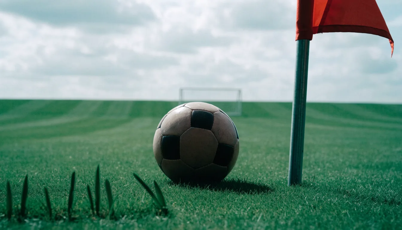 Ein Fußball liegt neben einer Eckfahne auf kurz gemähtem Rasen unter bewölktem Himmel.